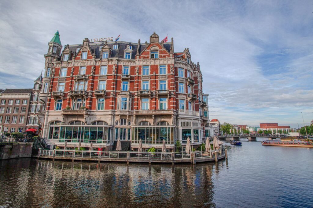 : Ornate red-brick building on Amsterdam canal island with boats and water reflections.